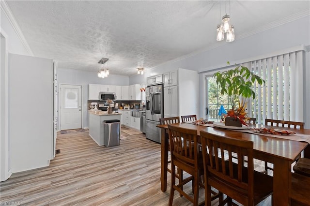 dining space with light wood-style floors, a textured ceiling, crown molding, and a chandelier