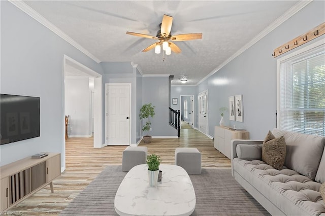 living area featuring crown molding, light wood-style floors, ceiling fan, stairway, and a textured ceiling