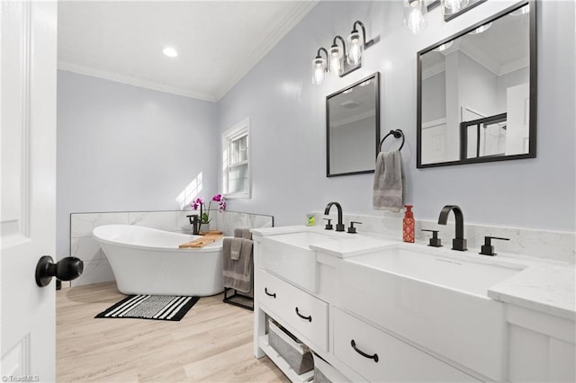 full bath with double vanity, ornamental molding, wood finished floors, a freestanding bath, and a sink