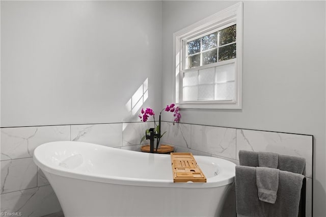 bathroom with a freestanding tub, tile walls, marble finish floor, and a wainscoted wall