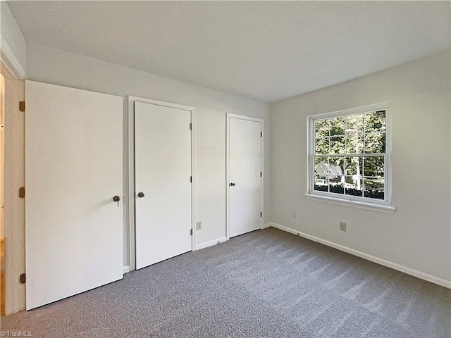 unfurnished bedroom featuring dark carpet, multiple closets, and a textured ceiling