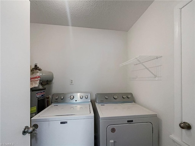 washroom with water heater, a textured ceiling, and washing machine and dryer