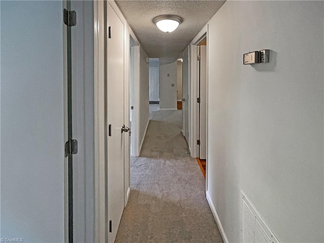 hallway featuring a textured ceiling and light colored carpet