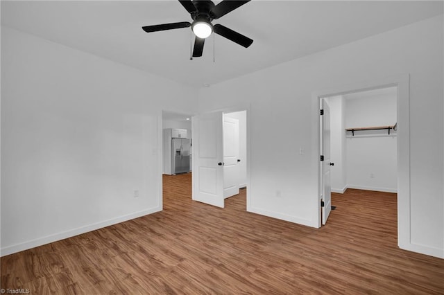 unfurnished bedroom featuring a closet, a walk in closet, wood-type flooring, stainless steel refrigerator with ice dispenser, and ceiling fan