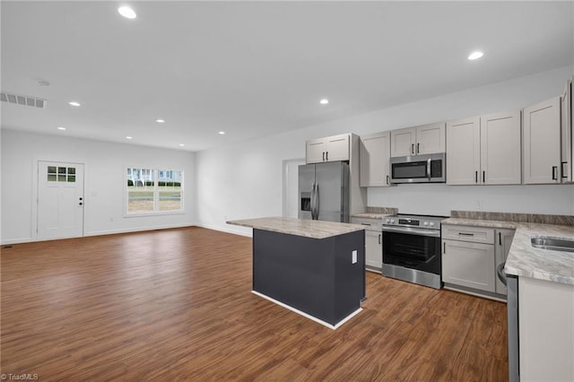 kitchen featuring stainless steel appliances, light stone countertops, dark hardwood / wood-style floors, a kitchen island, and gray cabinetry