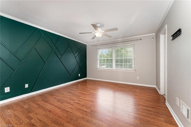 spare room with ceiling fan, ornamental molding, wood finished floors, baseboards, and a decorative wall