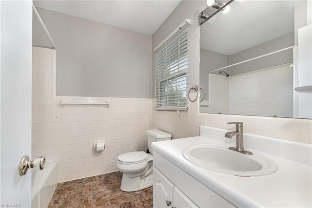 full bathroom with tile walls, toilet, vanity, a textured ceiling, and wainscoting