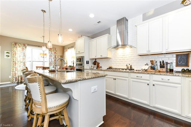 kitchen with sink, a kitchen island with sink, wall chimney range hood, and decorative light fixtures