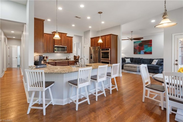 kitchen with appliances with stainless steel finishes, a sink, a peninsula, brown cabinets, and recessed lighting