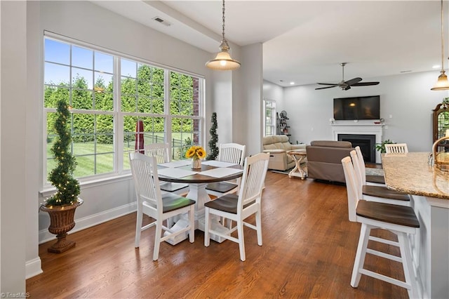 dining area featuring a fireplace, dark wood-type flooring, ceiling fan, and baseboards