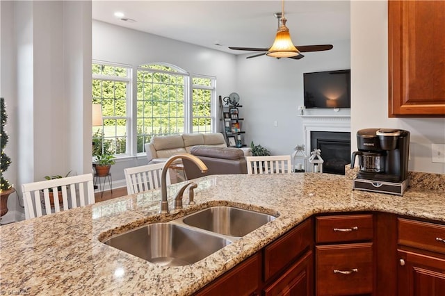 kitchen with a sink, light stone countertops, open floor plan, and a ceiling fan