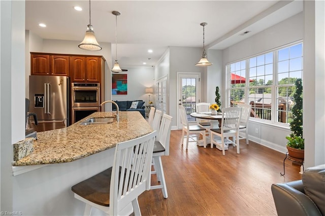 kitchen with appliances with stainless steel finishes, open floor plan, a kitchen breakfast bar, light stone counters, and a sink