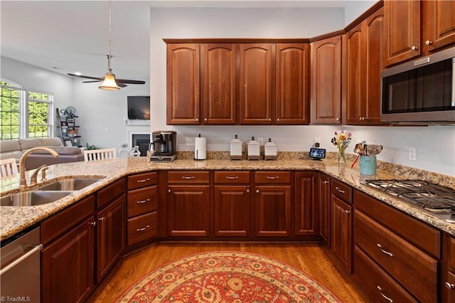 kitchen with stainless steel appliances, a sink, light wood finished floors, light stone counters, and recessed lighting