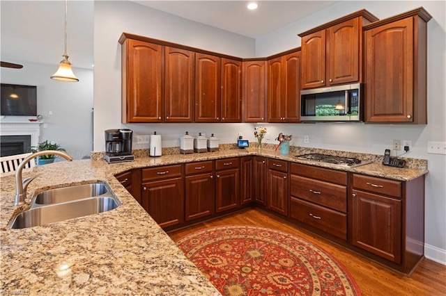kitchen with stainless steel appliances, a sink, wood finished floors, light stone countertops, and recessed lighting
