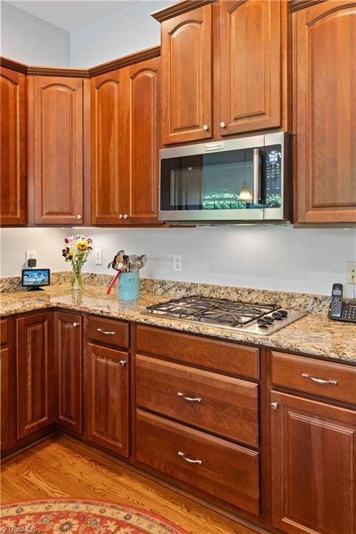 kitchen featuring appliances with stainless steel finishes, light wood-style flooring, light stone countertops, and brown cabinets