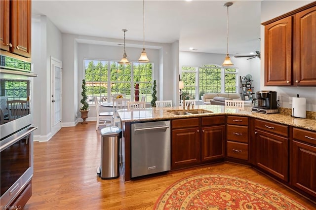 kitchen with a sink, appliances with stainless steel finishes, light wood-style floors, decorative light fixtures, and light stone countertops