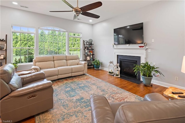living area featuring a ceiling fan, a glass covered fireplace, wood finished floors, baseboards, and recessed lighting