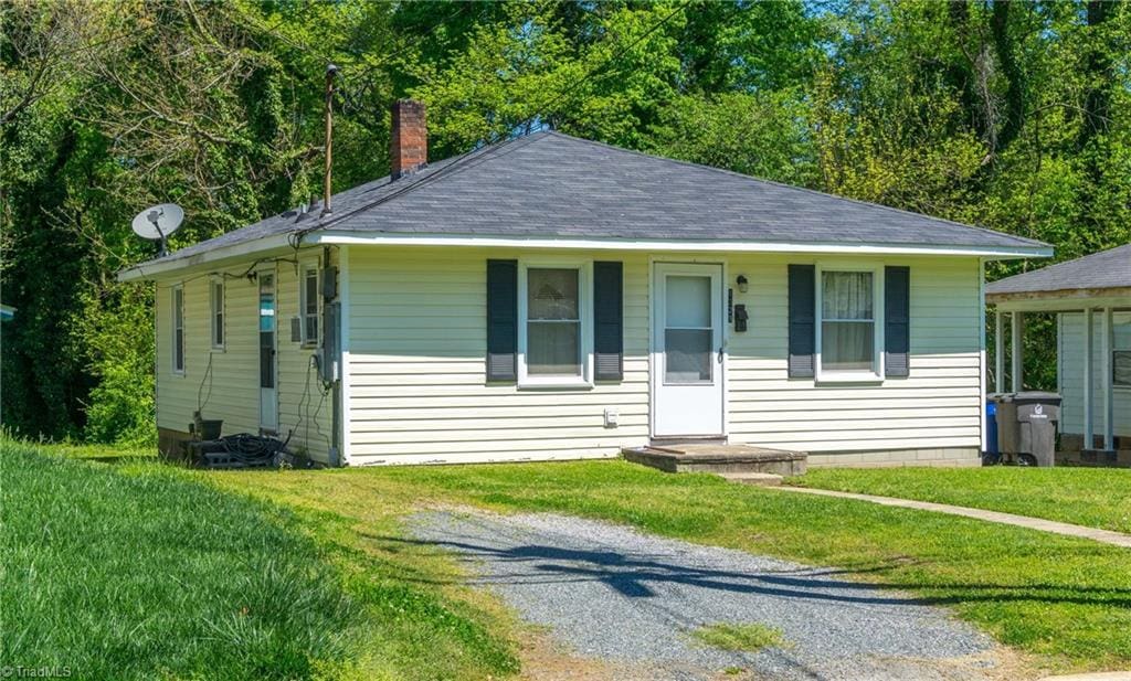 bungalow-style home with driveway, a shingled roof, a chimney, and a front yard