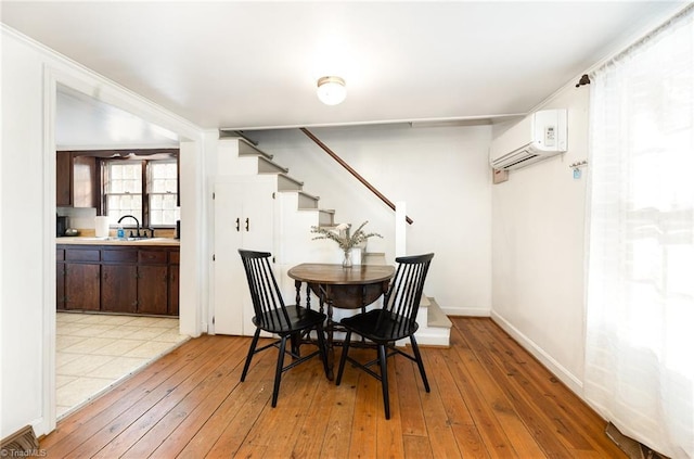 dining space featuring light wood-style flooring, visible vents, baseboards, stairway, and a wall mounted AC