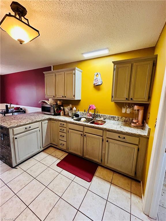 kitchen featuring sink, a textured ceiling, kitchen peninsula, and light tile patterned floors