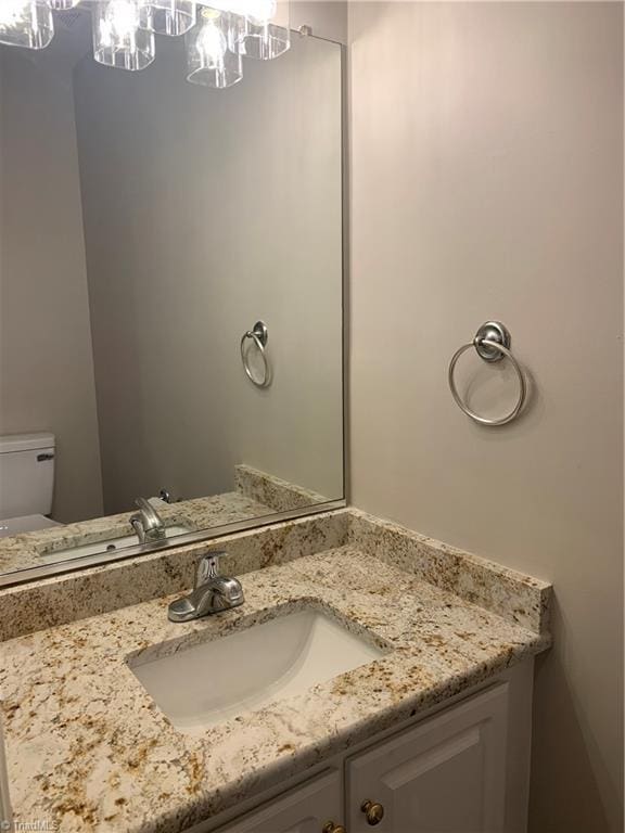 half bathroom with vanity, toilet, and a notable chandelier