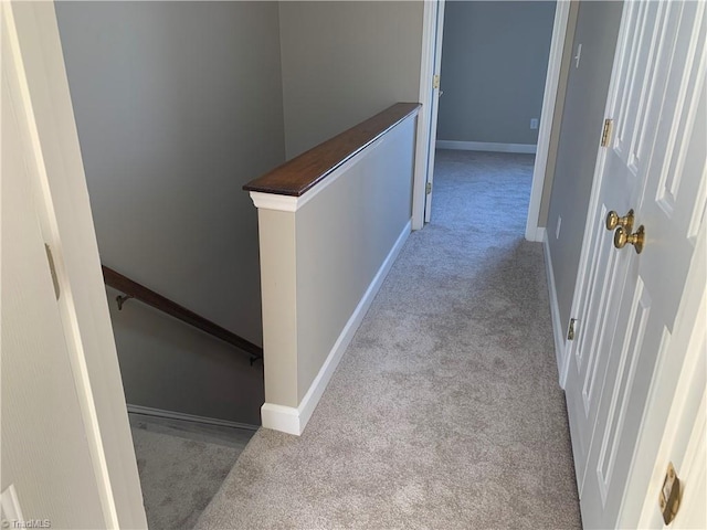 hallway featuring baseboards, carpet floors, and an upstairs landing