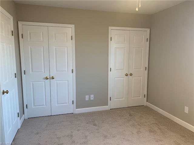 unfurnished bedroom featuring carpet, baseboards, and two closets