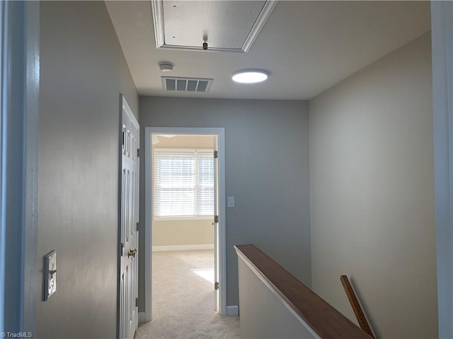 hallway with visible vents, light carpet, an upstairs landing, baseboards, and attic access