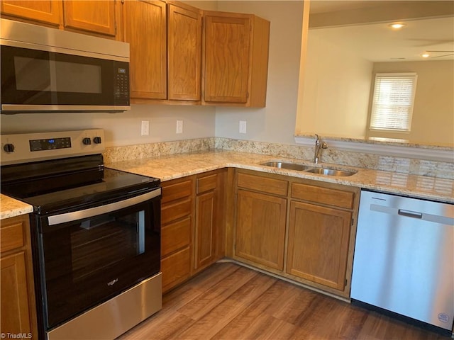 kitchen featuring light stone counters, brown cabinetry, light wood-style flooring, a sink, and appliances with stainless steel finishes