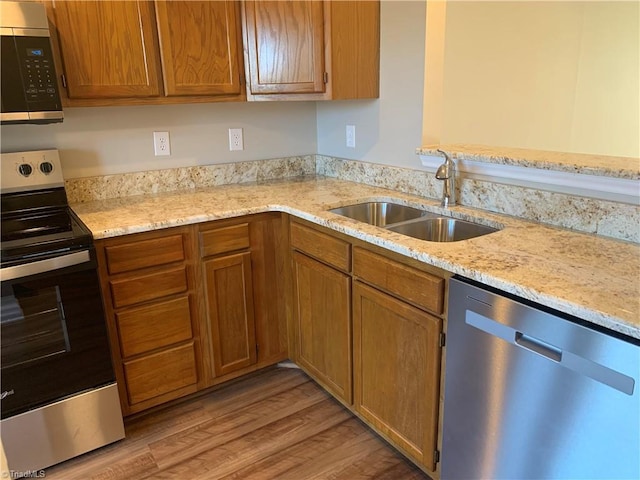 kitchen featuring a sink, stainless steel appliances, light stone counters, and light wood-style floors