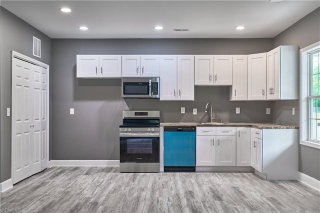 kitchen with white cabinets, appliances with stainless steel finishes, light wood-type flooring, and sink