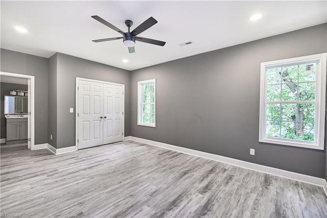 unfurnished bedroom with ceiling fan, a closet, ensuite bathroom, and light wood-type flooring