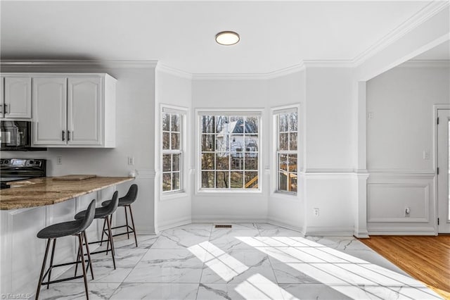 kitchen featuring white cabinetry, a healthy amount of sunlight, a kitchen breakfast bar, and electric stove