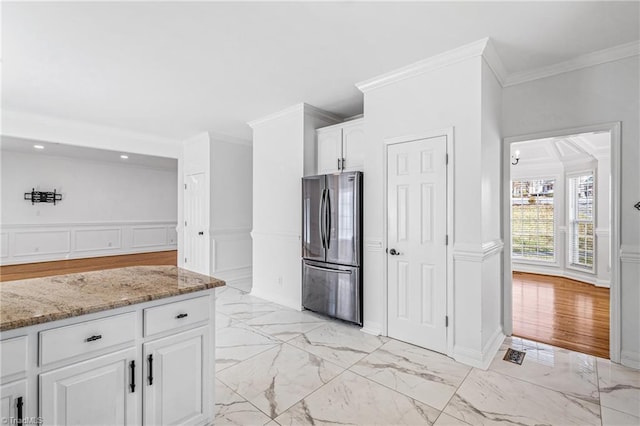 kitchen with white cabinetry, stainless steel fridge, light stone countertops, and crown molding