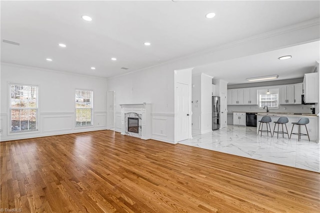 unfurnished living room with a premium fireplace, sink, crown molding, and light hardwood / wood-style flooring