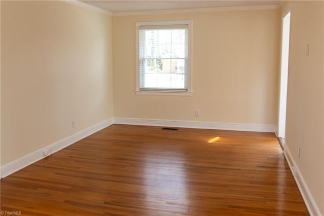 unfurnished room with visible vents, baseboards, wood finished floors, and ornamental molding