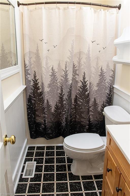 full bath with a wainscoted wall, curtained shower, toilet, and vanity