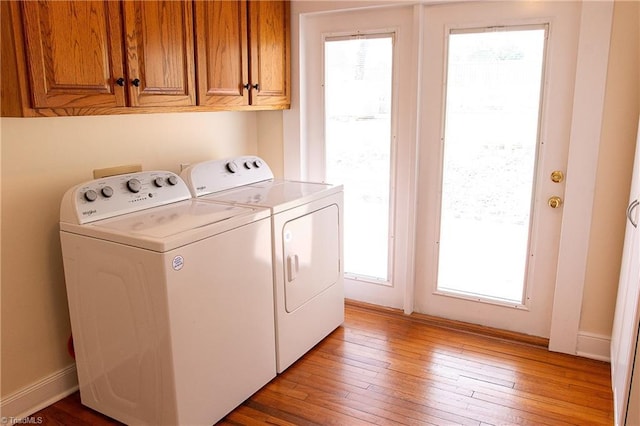 clothes washing area featuring washer and clothes dryer, cabinet space, baseboards, and light wood-style floors