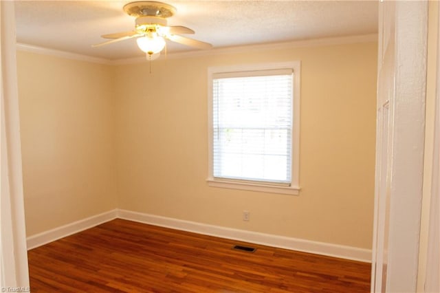 empty room with dark wood finished floors, crown molding, and baseboards