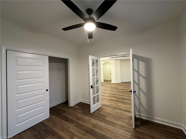 unfurnished bedroom featuring a closet, arched walkways, dark wood-style flooring, and baseboards