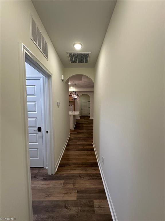 corridor with arched walkways, dark wood-style flooring, visible vents, and baseboards