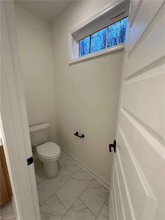 bathroom with toilet, marble finish floor, and baseboards