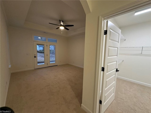 spare room featuring ceiling fan, arched walkways, light colored carpet, baseboards, and a raised ceiling