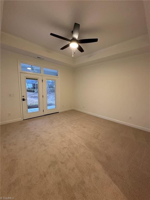 carpeted spare room with a raised ceiling, ceiling fan, and baseboards