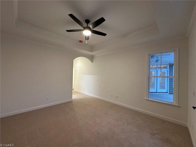 spare room featuring baseboards, a tray ceiling, arched walkways, and carpet flooring