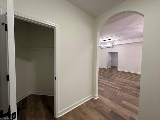 hall with dark wood-type flooring, arched walkways, and baseboards