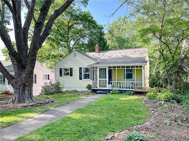 ranch-style house featuring roof with shingles, a chimney, a porch, and a front yard