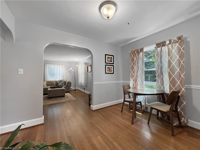 dining room featuring arched walkways, baseboards, and wood finished floors