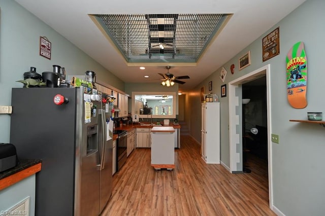 kitchen featuring a tray ceiling, light wood-style flooring, appliances with stainless steel finishes, and a ceiling fan