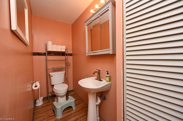 half bath with toilet, wood finished floors, and a sink